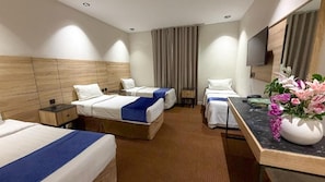 A hotel room with two beds, a desk, a flat-screen TV, and a vase with flowers. - Al Massa Al Ayam Hotel (Makkah)