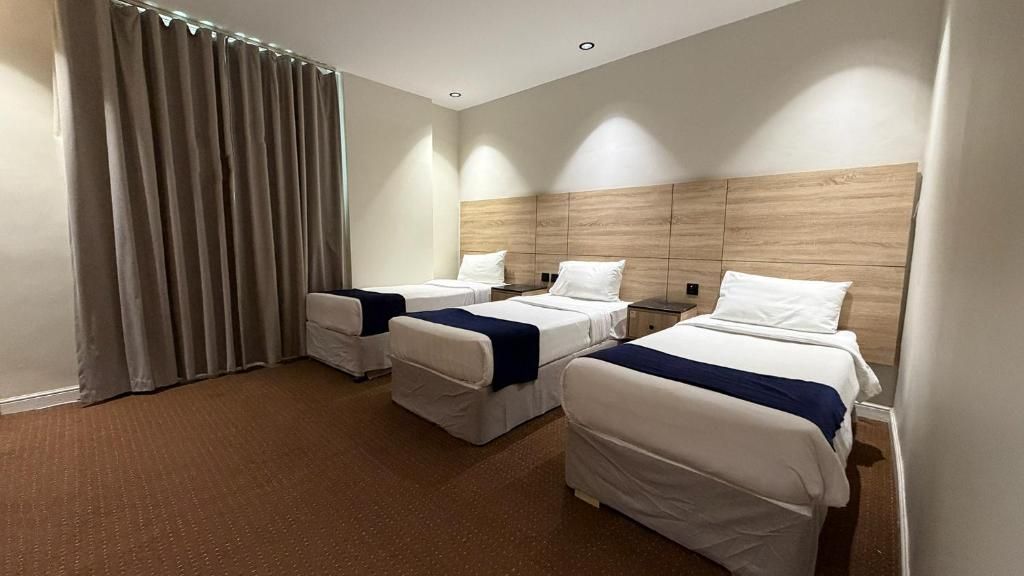 A hotel room with two single beds, a large window with curtains, and a wooden headboard.