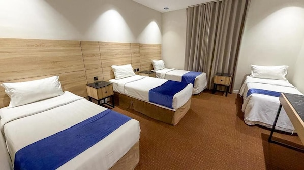 A hotel room with four beds arranged in a row, a wooden headboard, a small desk, and a window with curtains. - Al Massa Al Ayam Hotel (Makkah)