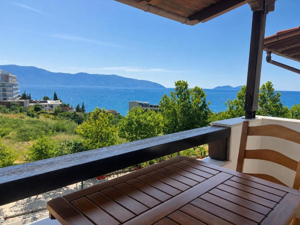 A wooden table and chair on a balcony with a view of a body of water and distant mountains.