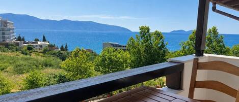 A wooden table and chair on a balcony with a view of a body of water and distant mountains.