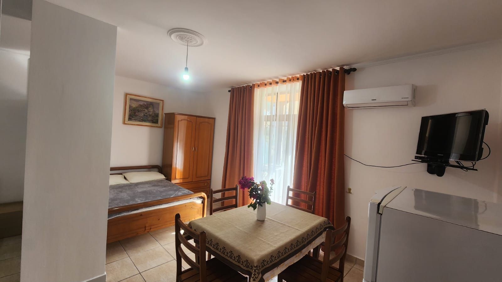 Ein Zimmer mit einem Bett, einem Tisch mit Stühlen, einem an der Wand montierten Fernseher und einer Klimaanlage.