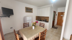 Un comedor con una mesa, sillas, televisor, refrigerador y una cocina con pileta y alacenas.