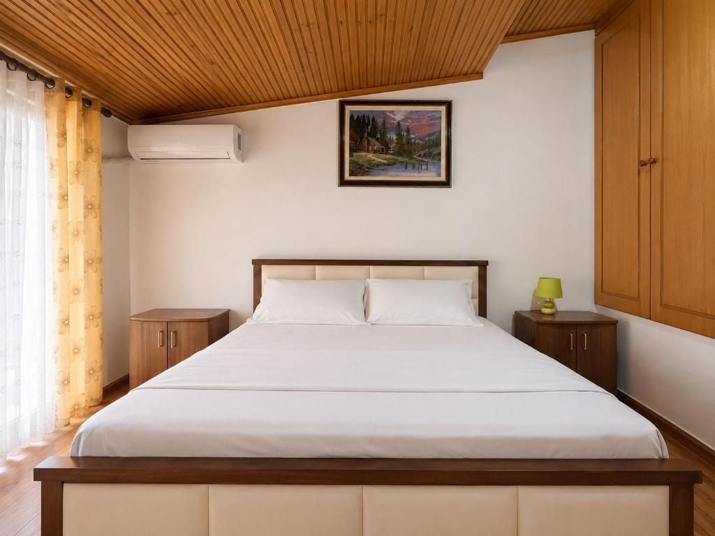A bedroom with a wooden ceiling, a bed with white bedding, a painting on the wall, and a nightstand with a lamp.