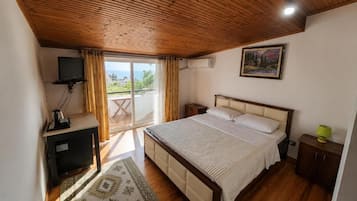 A bedroom with a bed, a television, a desk, a window with curtains, and a painting on the wall.