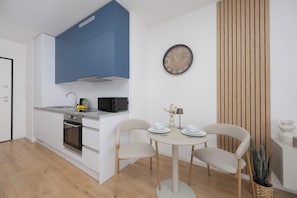 A modern kitchen with white cabinets, a blue upper section, and a dining area with a round table and two chairs. - Warsaw | Krochmalna 61 | Modern Studio | Air Conditioning (Warszawa)