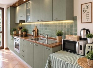 Una cucina con mobili verdi, un lavello, un forno a microonde e un tavolo con tovaglia a quadri.