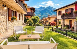 Un cortile con edifici in pietra, arredi bianchi e vista sulle montagne.