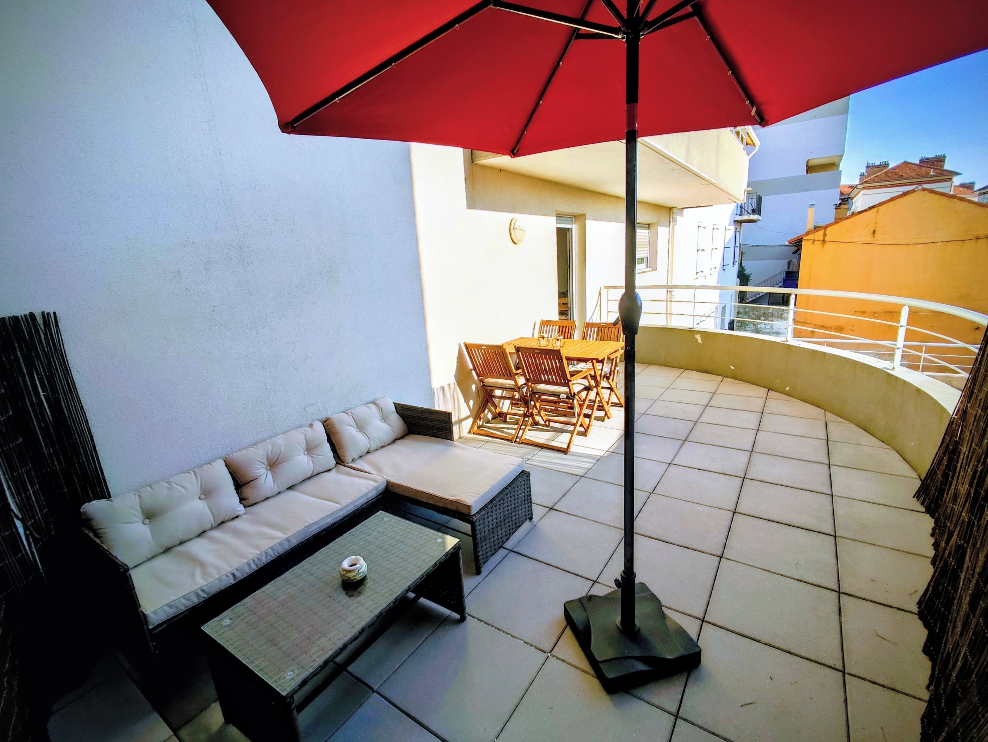 A patio with a sofa, a table, and a red umbrella.