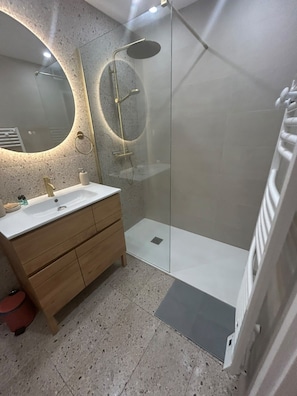 Un baño moderno con ducha de vidrio, espejo redondo y tocador de madera.