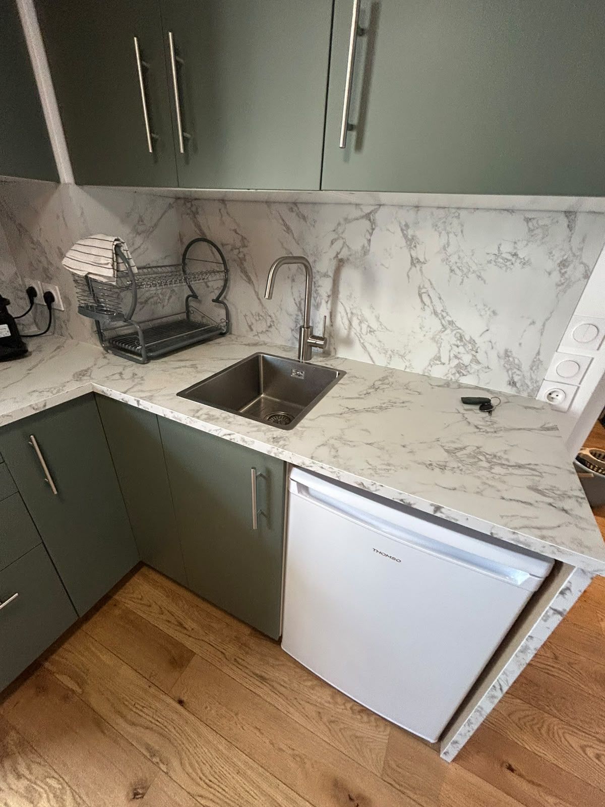 A compact kitchen with a built-in dishwasher, a sink, and a marble backsplash.