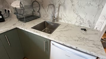A compact kitchen with a built-in dishwasher, a sink, and a marble backsplash.