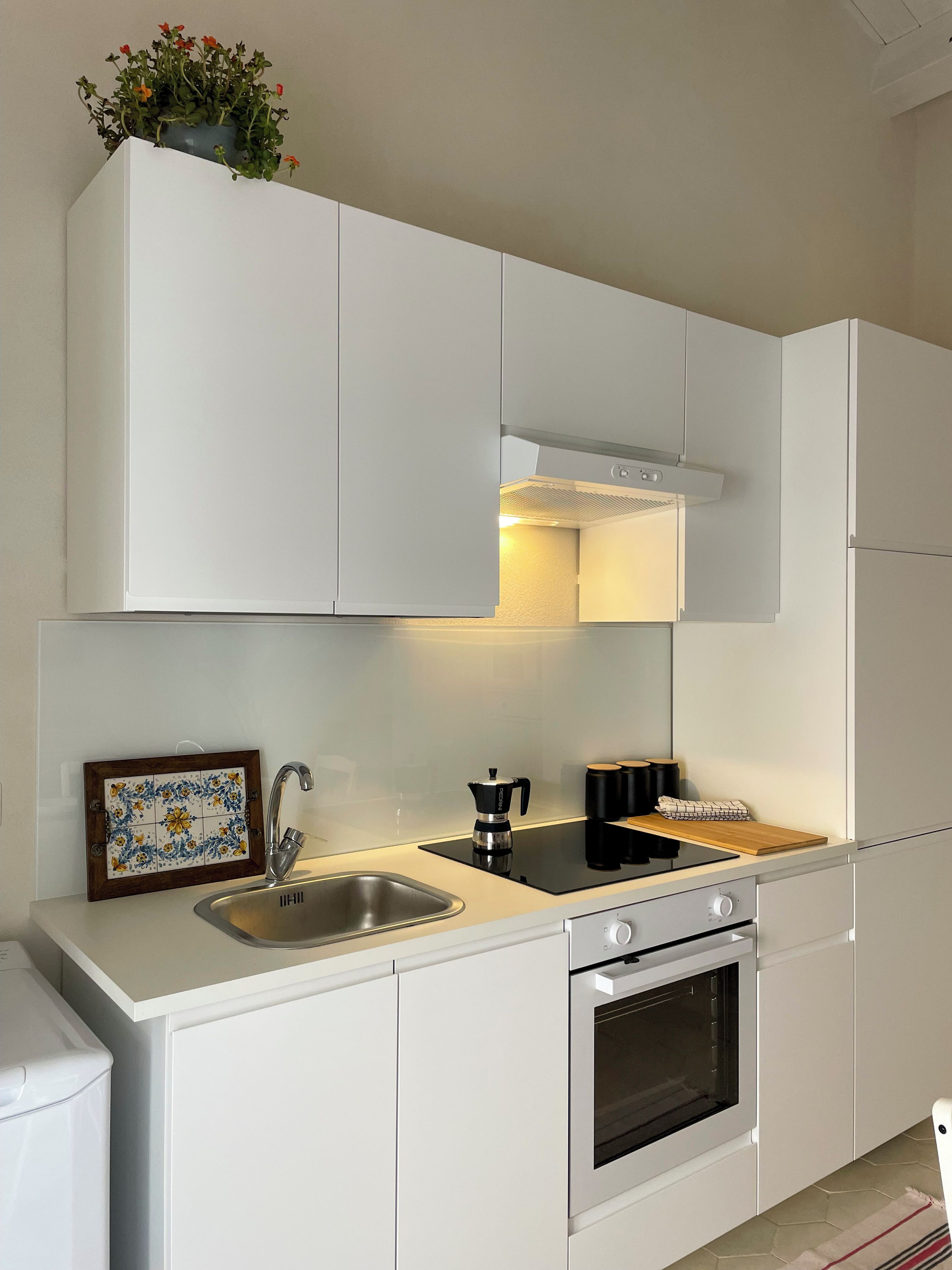 Une cuisine moderne avec des meubles blancs, un évier en acier inoxydable, une plaque de cuisson à induction noire et un four encastré.