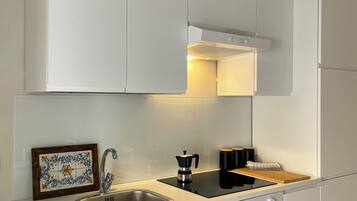 Une cuisine moderne avec des meubles blancs, un évier en acier inoxydable, une plaque de cuisson à induction noire et un four encastré.