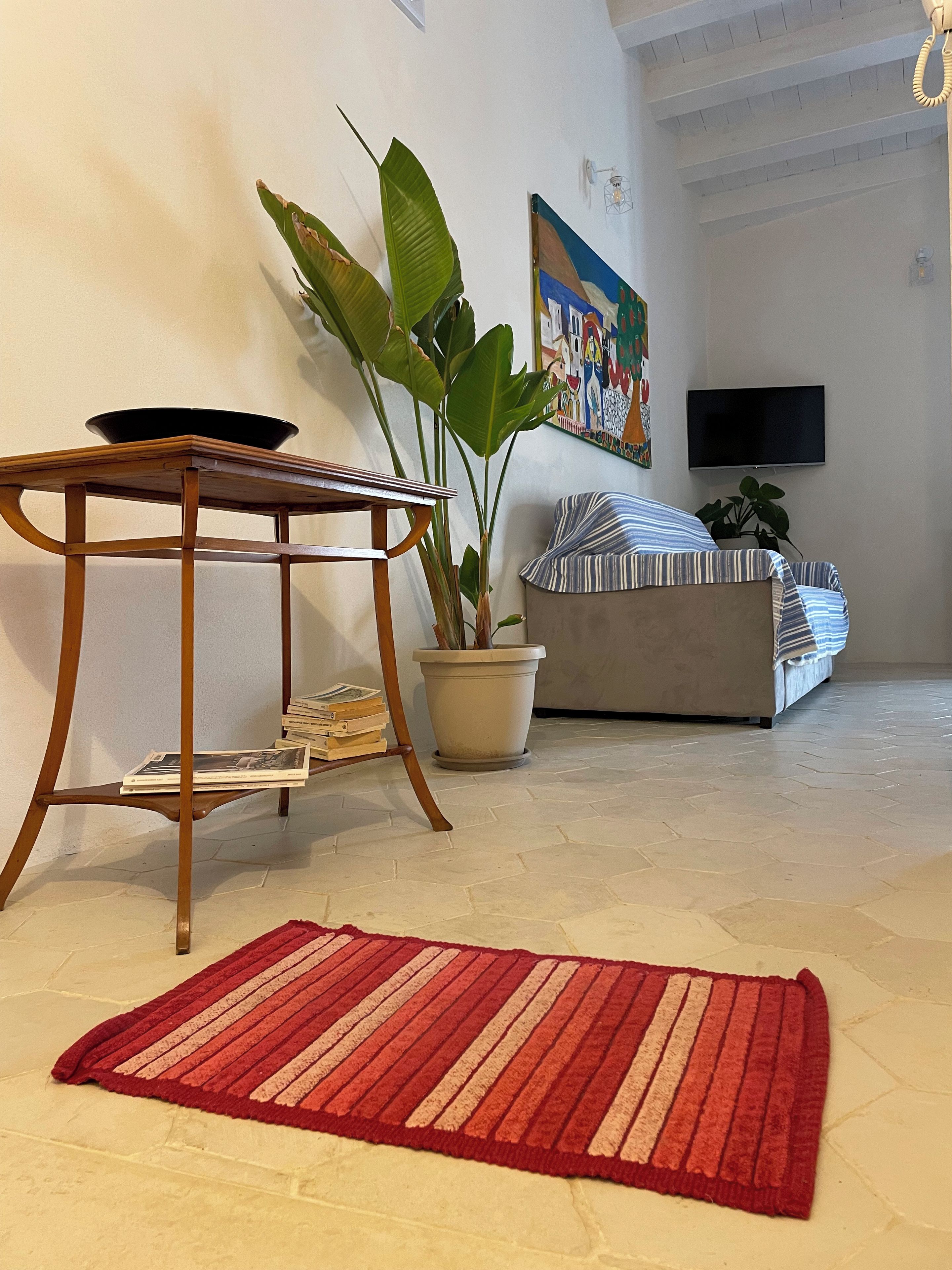 Un salon avec une table en bois, une plante en pot, un canapé et un tapis rouge.