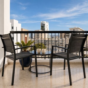 A balcony with two chairs and a table, a potted plant, and a view of buildings. - Urban Habitat Executive Suites (Nicosia)