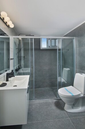 Un baño moderno con cabina de ducha de vidrio, un lavabo blanco y un inodoro.
