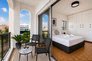 Un dormitorio moderno con cama, zona de estar y balcón con planta y mesa.