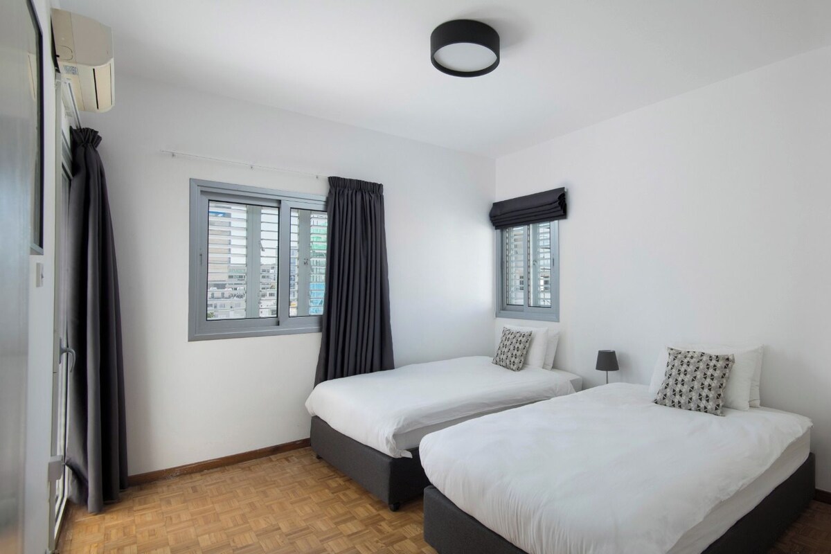Una habitación con dos camas, una ventana, una lámpara en el techo y una puerta.