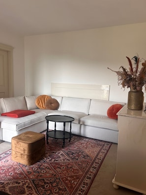 Ein Wohnzimmer mit Sofa, Hocker, Couchtisch und einem gemusterten Teppich.