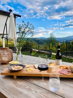 Mesa al aire libre con una botella de vino, queso, frutos secos, galletas y un vaso de agua.