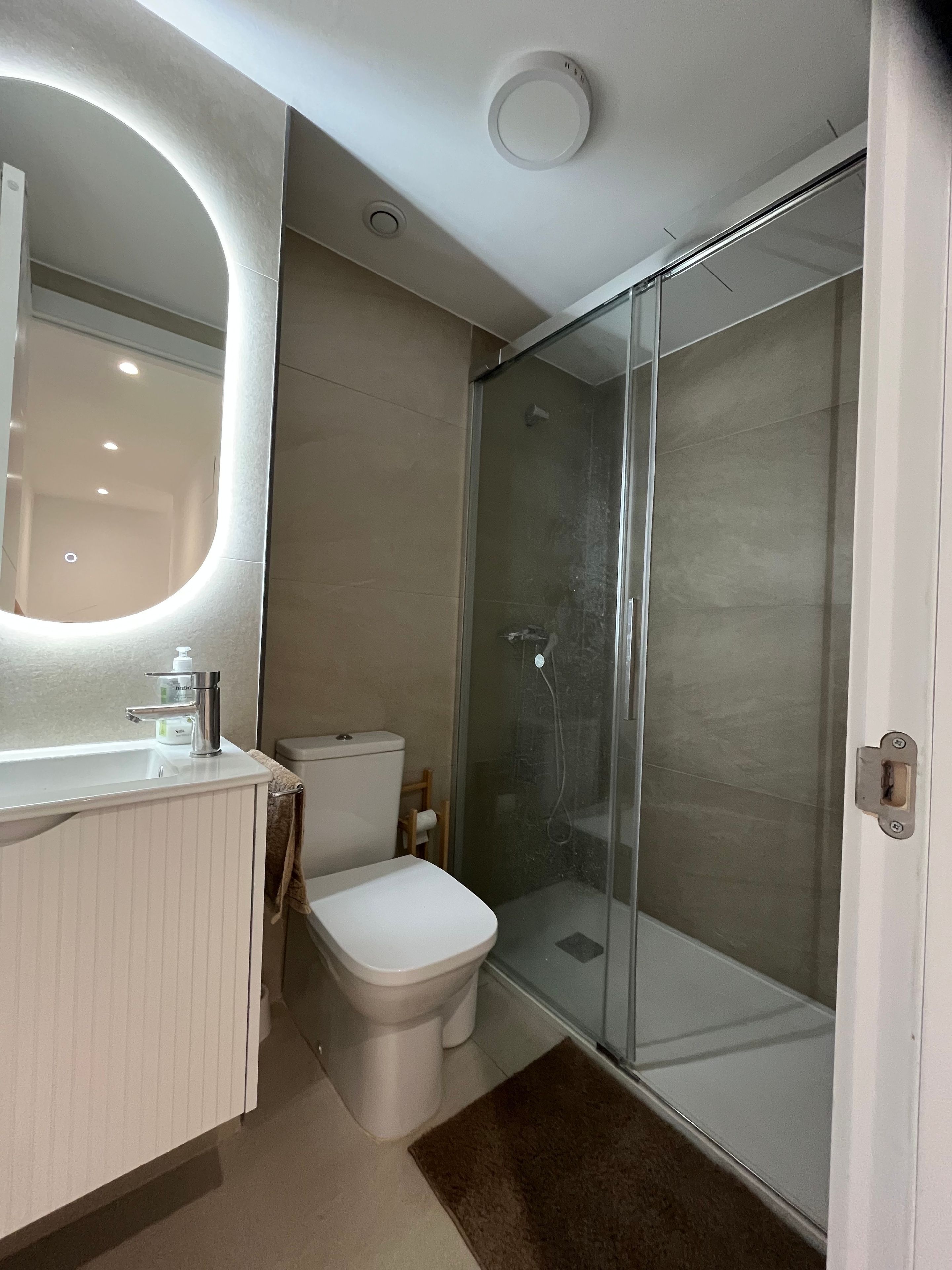 Une salle de bain comprenant des toilettes, un lavabo, un miroir et une douche fermée par une paroi de verre.