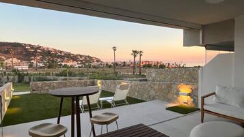 Um pátio moderno ao ar livre com mesa e cadeiras, paredes de pedra e vista para uma vila no topo do morro.
