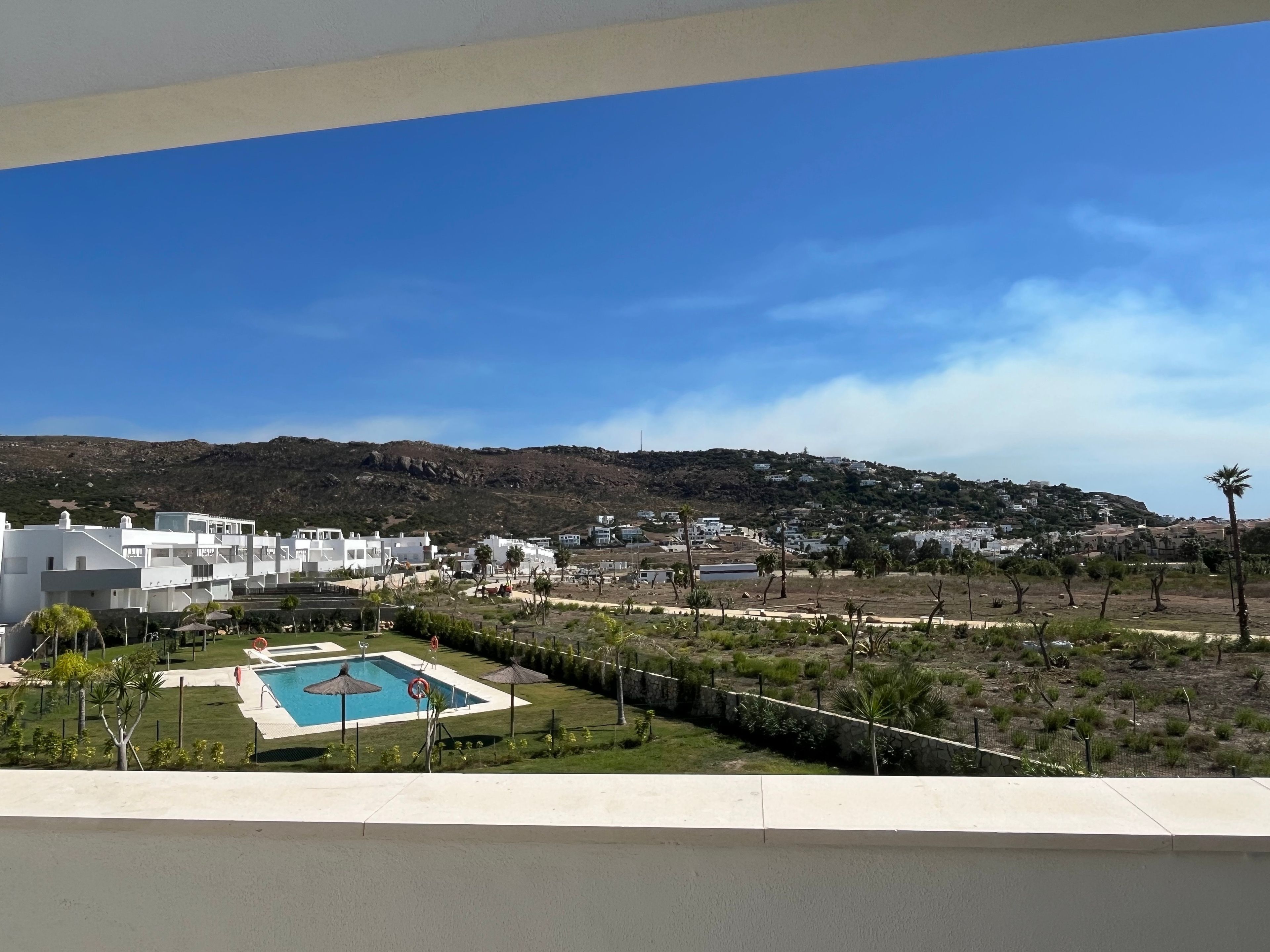 Área residencial com edifícios brancos, piscina e paisagem montanhosa ao fundo.