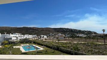 Área residencial com edifícios brancos, piscina e paisagem montanhosa ao fundo.