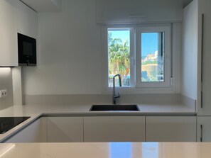 A modern kitchen with a built-in sink, a flat-screen TV mounted above it, and a window providing a view of palm trees and buildings.