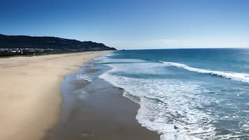Une plage avec un ciel dégagé, des vagues qui se rapprochent du rivage et une montagne lointaine.