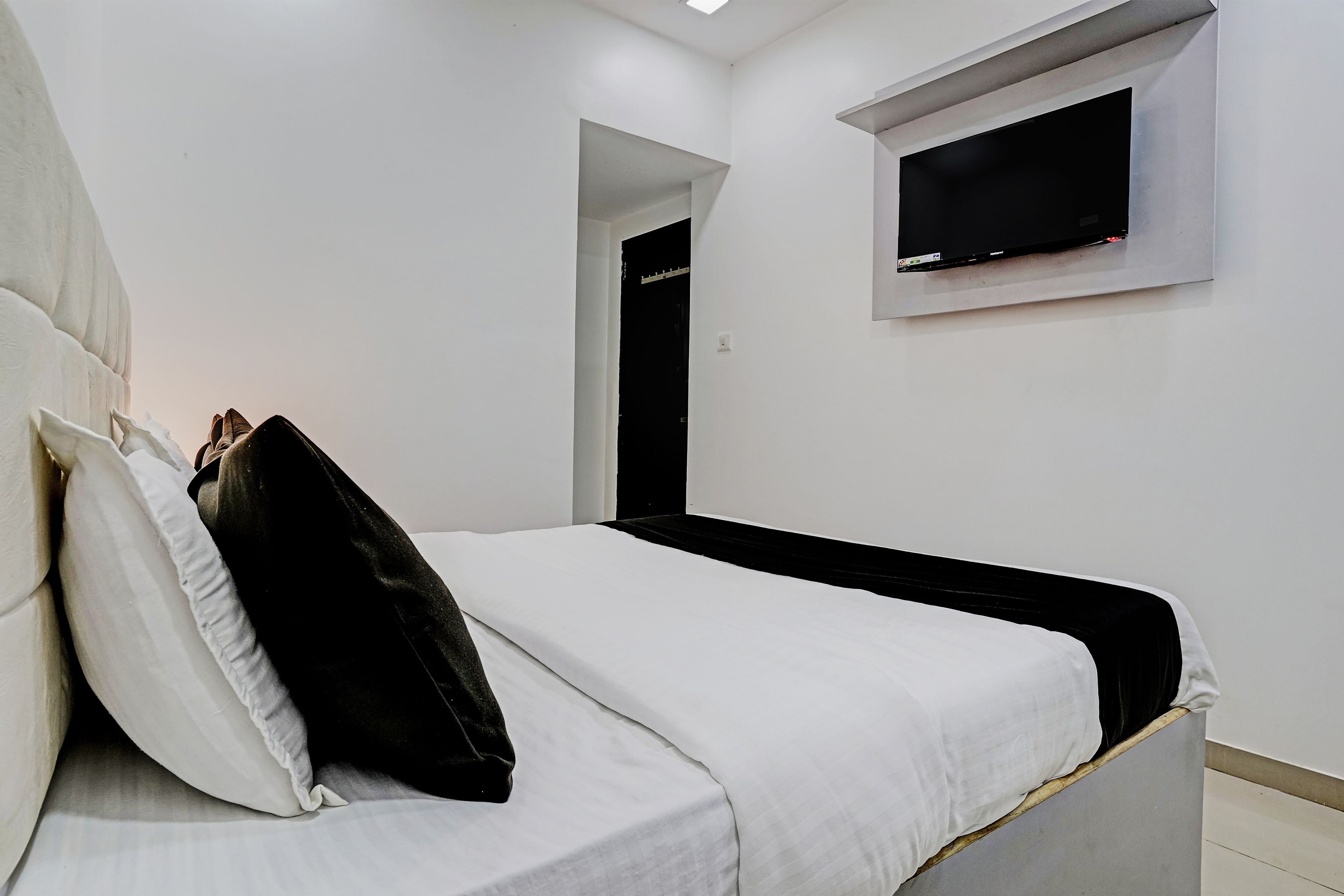 Un dormitorio con una cama, un televisor en la pared y una puerta que da a otra habitación.