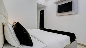 Un dormitorio con una cama, un televisor en la pared y una puerta que da a otra habitación.