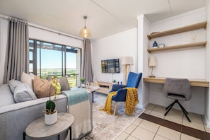 A modern living room with a sofa, armchairs, a small table with a plant, a TV, and a desk with a lamp. - Haus 189 Dainfern- Pool Play Area Power Backup (Johannesburg)