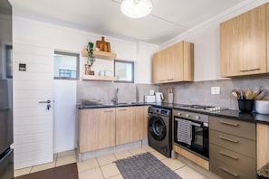 A modern kitchen with wooden cabinets, a built-in washing machine, and a stove. - Haus 189 Dainfern- Pool Play Area Power Backup (Johannesburg)