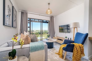 Ein modernes Wohnzimmer mit Sofa, Sessel, Couchtisch und Fernseher.