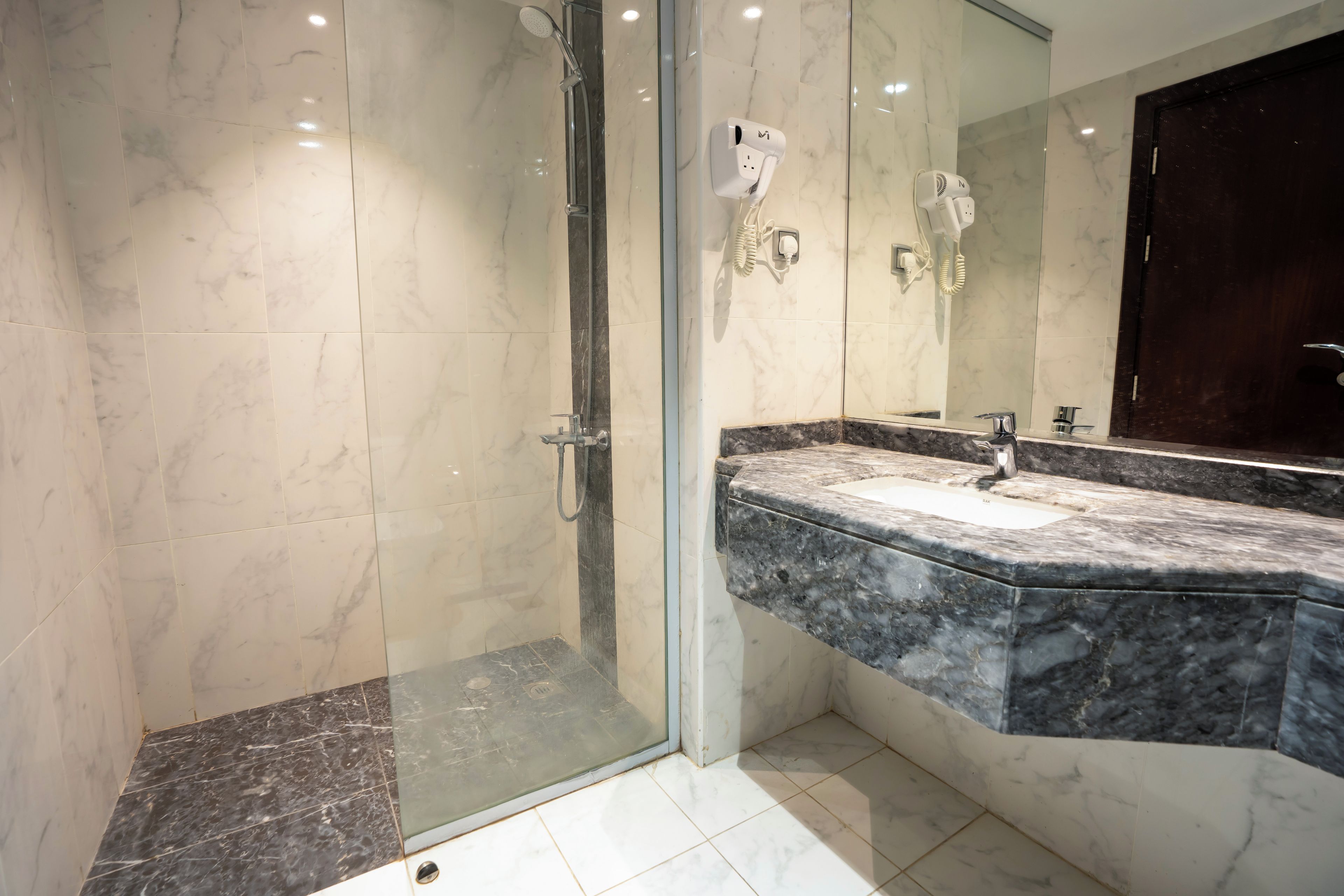 Une salle de bain moderne dotée d’une douche en verre, d’un sol carrelé en marbre et d’un plan de travail en granit avec un évier.