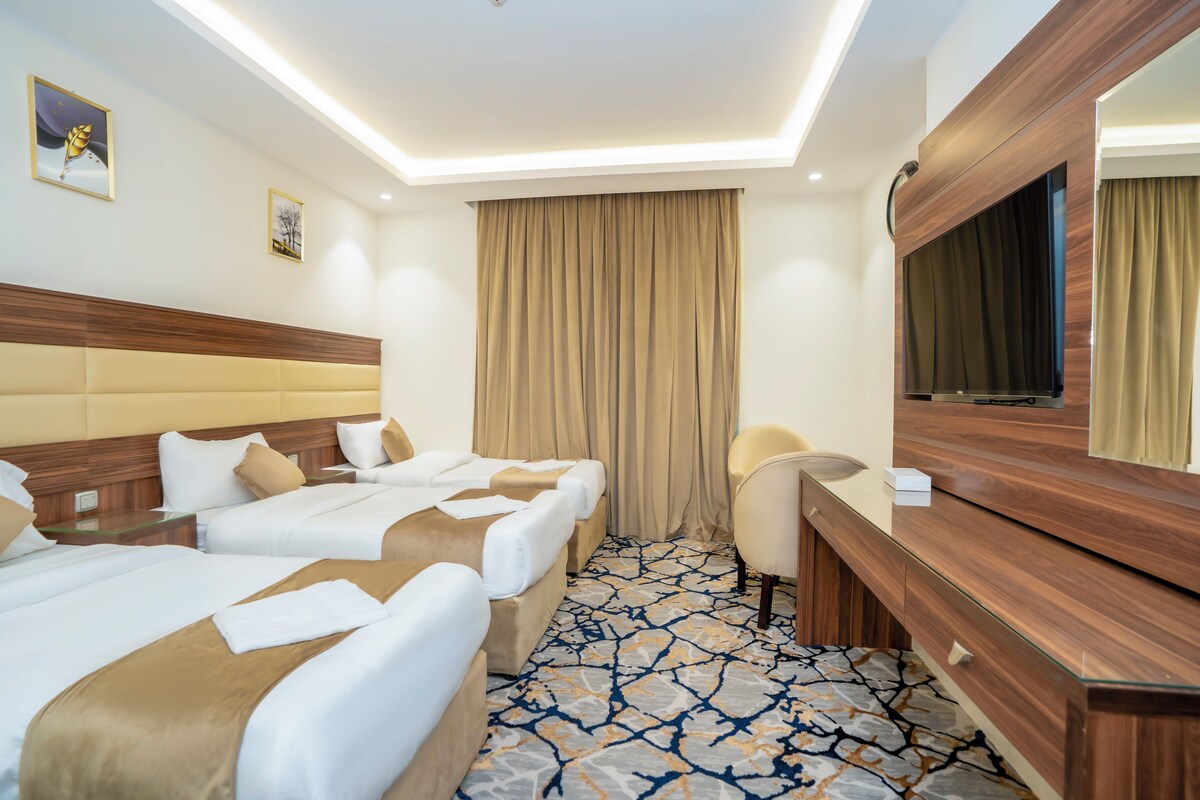 A hotel room with two beds, a desk, a chair, a large mirror, and a patterned carpet.