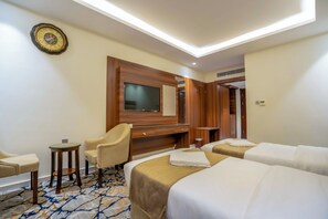 A hotel room with two beds, a desk, a chair, a TV, and a wooden wardrobe. - Manazil Al Maqam Hotel (Makkah)