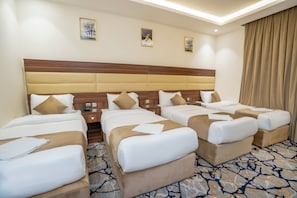 A hotel room with four beds arranged in a row, a wooden headboard, a patterned carpet, and a large window with curtains. - Manazil Al Maqam Hotel (Makkah)