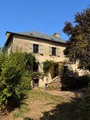 Ein zweistöckiges Haus mit einer Steintreppe, die zum Eingang führt, umgeben von viel Grün.