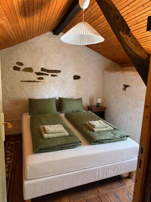 Ein Schlafzimmer mit Holzbalkendecke, einem Bett mit grüner Bettwäsche und einer weißen Wand mit Beschädigungen.