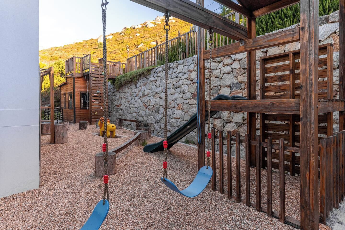 A playground with swings, a slide, and a wooden playhouse.