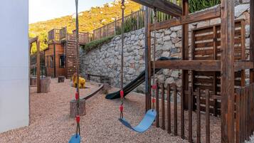 A playground with swings, a slide, and a wooden playhouse.