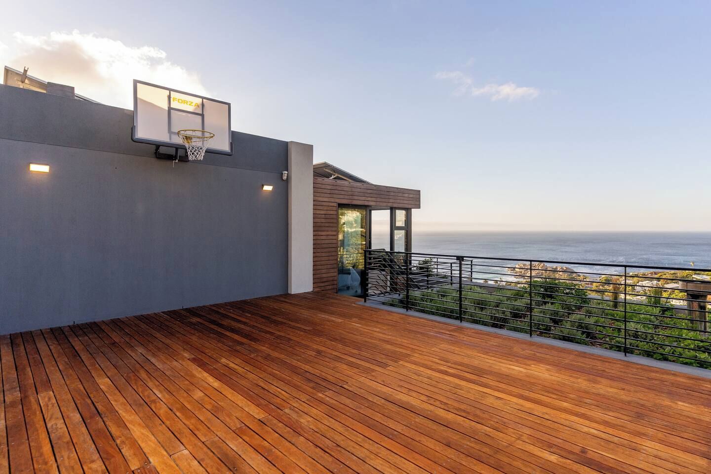 A wooden deck with a basketball hoop, a glass door leading to a covered area, and a view of the ocean.