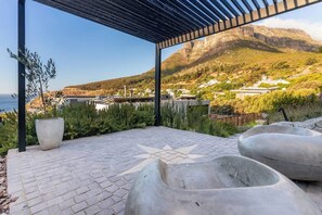 An outdoor patio with a star-shaped design, a pergola, and a view of a mountainous landscape with buildings in the distance. - Hill House heated infinity pool & kids' paradise (Cape Town)