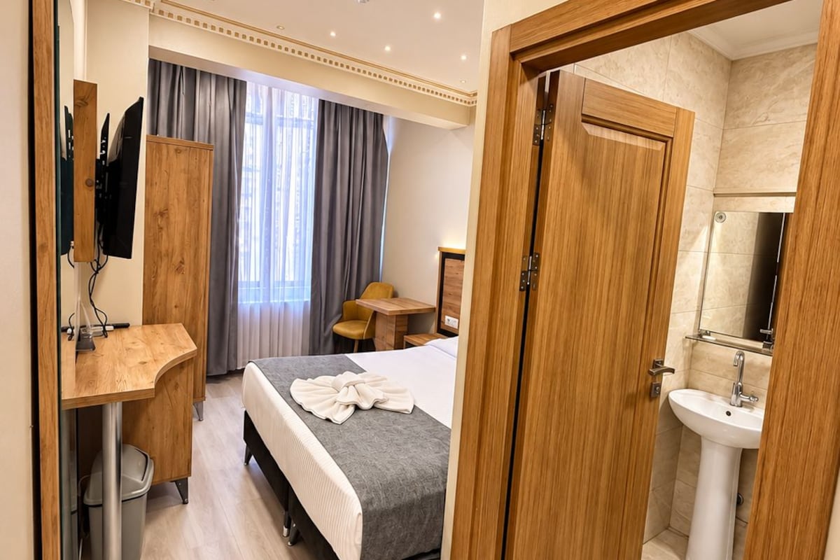 A hotel room with a bed, a desk, a chair, a wardrobe, and a bathroom with a sink.