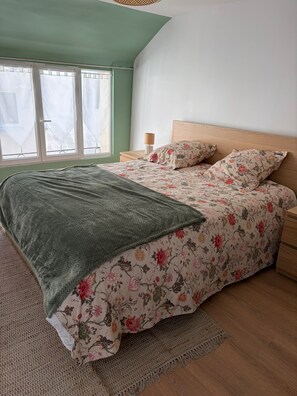 A bedroom with a bed, a nightstand, a lamp, and a window with curtains. - ⚓ Charming fisherman's cottage in the heart of Saint-Vaast-la-Hougue (Saint-Vaast-la-Hougue)
