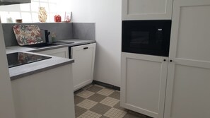 A kitchen with white cabinets, a microwave, and a tiled floor. - ⚓ Charming fisherman's cottage in the heart of Saint-Vaast-la-Hougue (Saint-Vaast-la-Hougue)