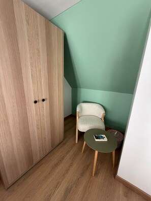 A room with a wooden wardrobe, a chair, a small round table, and a green wall. - ⚓ Charming fisherman's cottage in the heart of Saint-Vaast-la-Hougue (Saint-Vaast-la-Hougue)